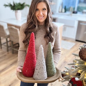 May include: Three crocheted Christmas trees in a wooden tray. The trees are red, gray, and green.