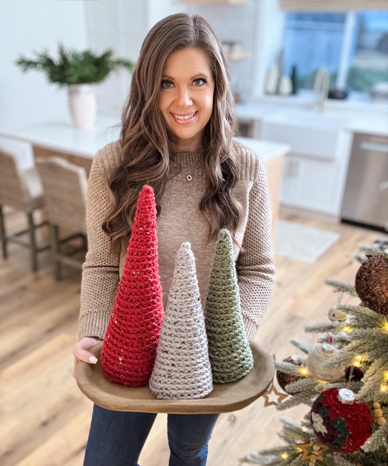 May include: Three crocheted Christmas trees in a wooden tray. The trees are red, gray, and green.