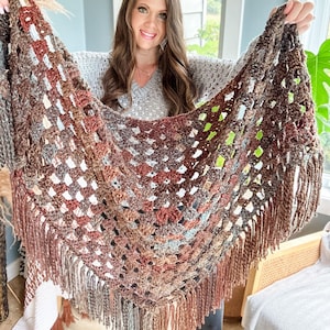 May include: A brown, grey, and blue crocheted shawl with fringe. The shawl is made with a square stitch pattern.