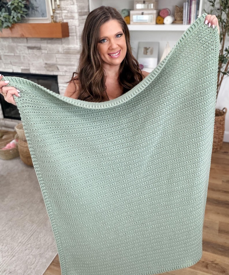 Puede incluir: Una manta rectangular de ganchillo en color verde salvia que presenta un patr&oacute;n de puntos texturizados consistente en todo el cuerpo y un borde ligeramente m&aacute;s grueso y definido. El tejido es uniforme y de construcci&oacute;n densa.