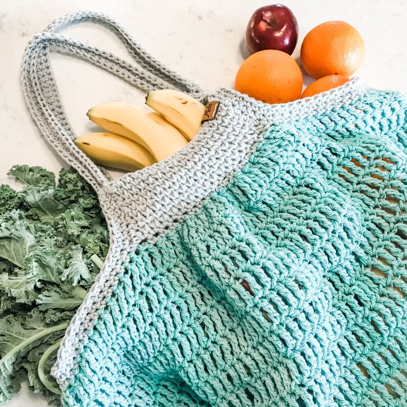 May include: A light blue and gray crocheted tote bag with a gray handle. The bag is filled with bananas and fruit. The bag has a tag that says "Joy".