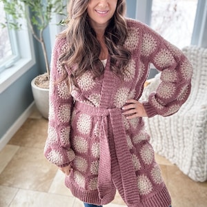 May include: A long-sleeved, pink and white crocheted cardigan with a tie belt. The cardigan has a textured, puffy design.