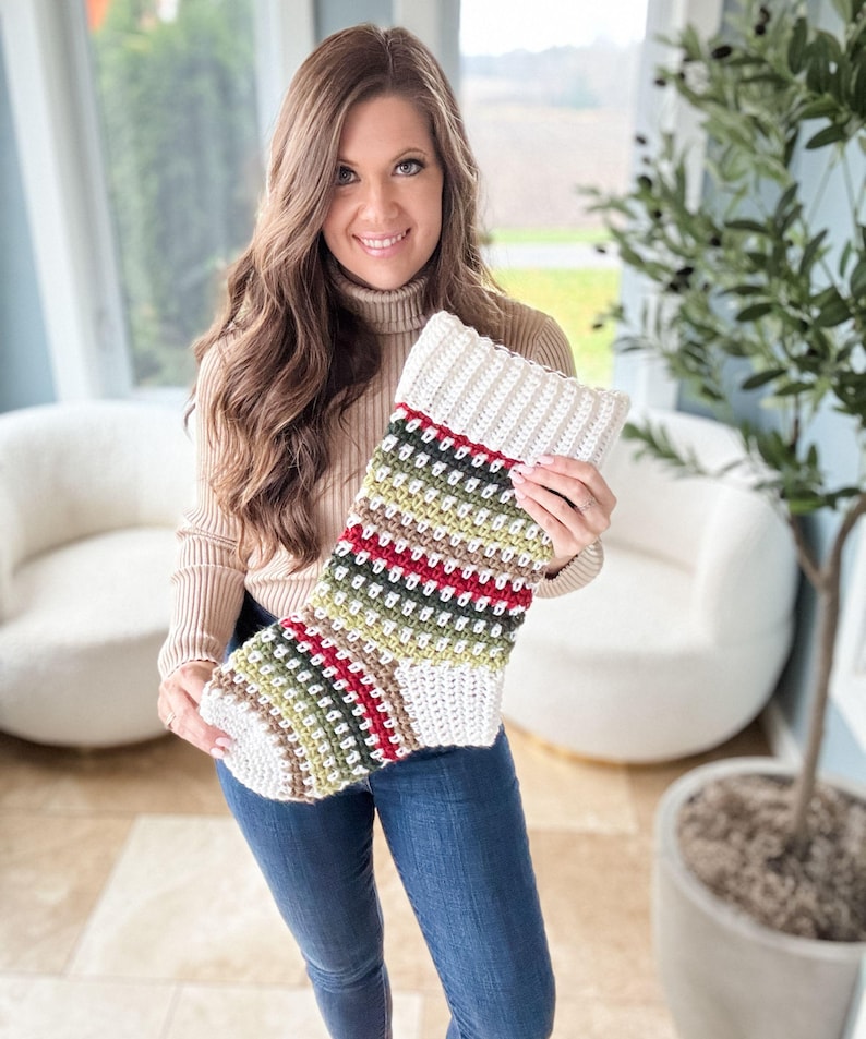 May include: A hand-crocheted Christmas stocking with a cream-coloured cuff and a body featuring stripes of red, green, and cream. The stocking has a textured stitch, creating a cosy and festive look. The overall design is a classic holiday decoration.