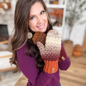 Peut inclure: Une paire de mitaines crochet&eacute;es &agrave; la main, dans un d&eacute;grad&eacute; de couleurs allant du cr&egrave;me au bordeaux, avec un motif de point textur&eacute;. Les poignets sont de couleur orange uni. Chaque mitaine a une petite &eacute;tiquette ronde marron.