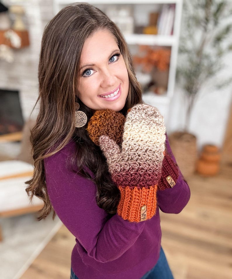 Peut inclure: Une paire de mitaines crochet&eacute;es &agrave; la main, dans un d&eacute;grad&eacute; de couleurs allant du cr&egrave;me au bordeaux, avec un motif de point textur&eacute;. Les poignets sont de couleur orange uni. Chaque mitaine a une petite &eacute;tiquette ronde marron.
