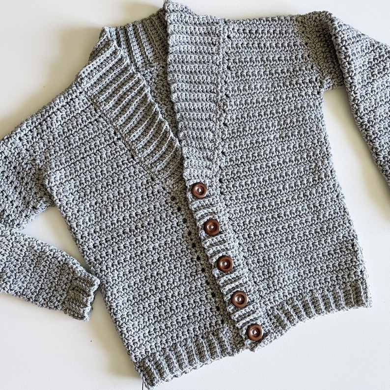 May include: A grey crocheted cardigan with a V-neck and wooden buttons.