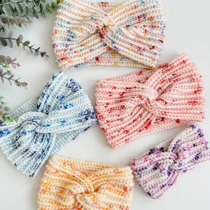 May include: Five crocheted headbands in different colors and patterns. The headbands are all made with a twisted knot design. The colors include white with multi-colored flecks, light blue with white flecks, pink with white flecks, orange with white flecks, and purple with white flecks.