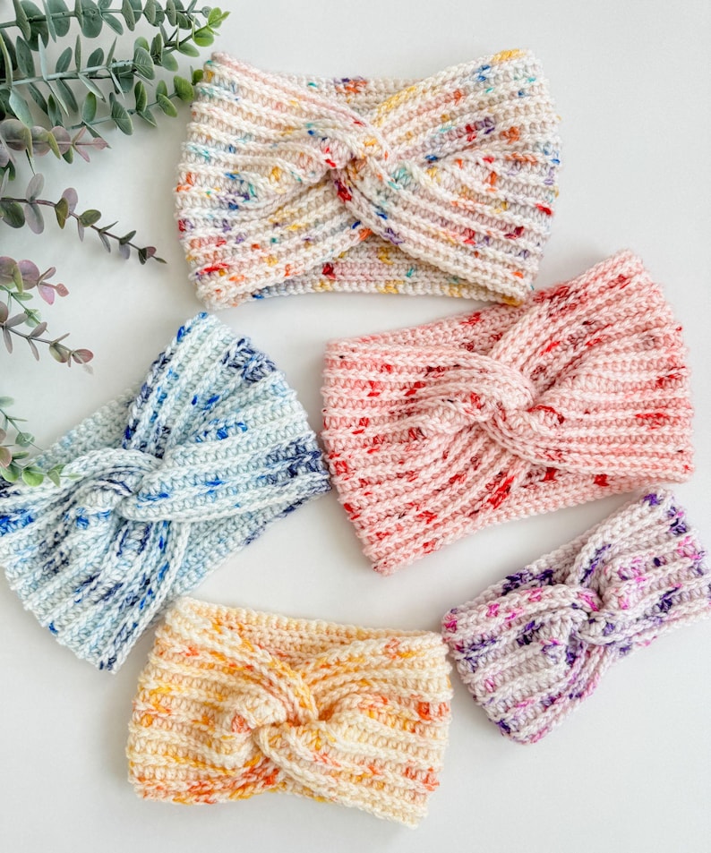 May include: Five crocheted headbands in different colors and patterns. The headbands are all made with a twisted knot design. The colors include white with multi-colored flecks, light blue with white flecks, pink with white flecks, orange with white flecks, and purple with white flecks.