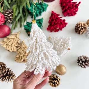 K&ouml;nnte beinhalten: Handgefertigte Weihnachtsbaumschmuck in Wei&szlig;, Gold, Gr&uuml;n und Rot. Die Ornamente, mit goldenen Akzenten, sind als Weihnachtsb&auml;ume geformt. Tannenzapfen und andere festliche Dekorationen sind ebenfalls zu sehen.