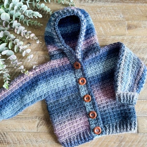 Pode incluir: Um cardigan de crochê com capuz listrado azul e roxo com botões de madeira.
