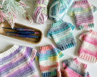 Puede incluir: Una colección de seis jerséis de ganchillo coloridos en varios patrones y colores, incluyendo rosa, morado, azul, verde y blanco. Los jerséis están dispuestos sobre una superficie blanca.