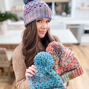 May include: Three crocheted hats with pom-poms in shades of purple, blue, and red. Each hat has a brown leather patch with the text "JM Handmade" on it.