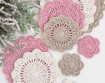 May include: A collection of handmade crochet doilies and coasters in various sizes and colors. The set includes round doilies in pink, cream, and tan, along with smaller, flower-shaped coasters. The crochet work features a scalloped edge design.
