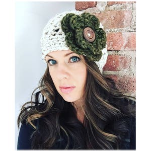 May include: A white crocheted beanie with a large green crocheted flower and a brown button.