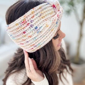 May include: A white crocheted headband with a colorful speckled pattern. The headband is tied in a knot on top of the head.