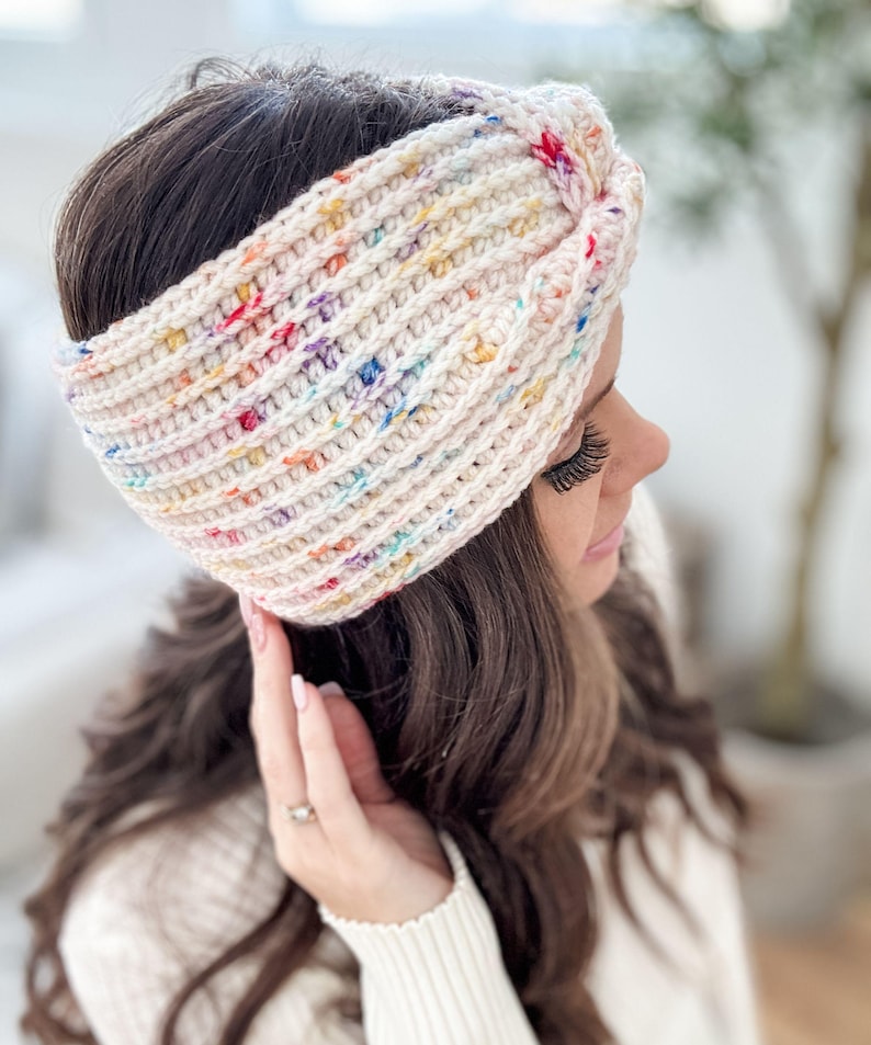 May include: A white crocheted headband with a colorful speckled pattern. The headband is tied in a knot on top of the head.