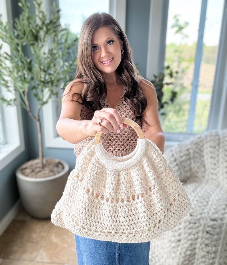 May include: A white crocheted tote bag with a wooden handle. The bag has a scalloped edge and a woven design.