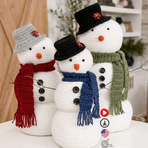 Pode incluir: Três bonecos de neve de crochê com olhos de botão pretos, narizes de cenoura laranja e corpos de botão pretos. Cada boneco de neve usa um cachecol e um chapéu de cores diferentes. Os chapéus são cinza, preto e preto. Os cachecóis são vermelho, azul e verde.