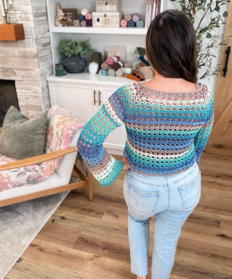 May include: A crochet top with long sleeves in shades of blue, turquoise, brown, and white. The open-weave design reveals the skin beneath. The top is paired with light blue jeans.