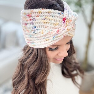 May include: A white crochet headband with a colorful confetti pattern. The headband is tied in a knot on top of the head.