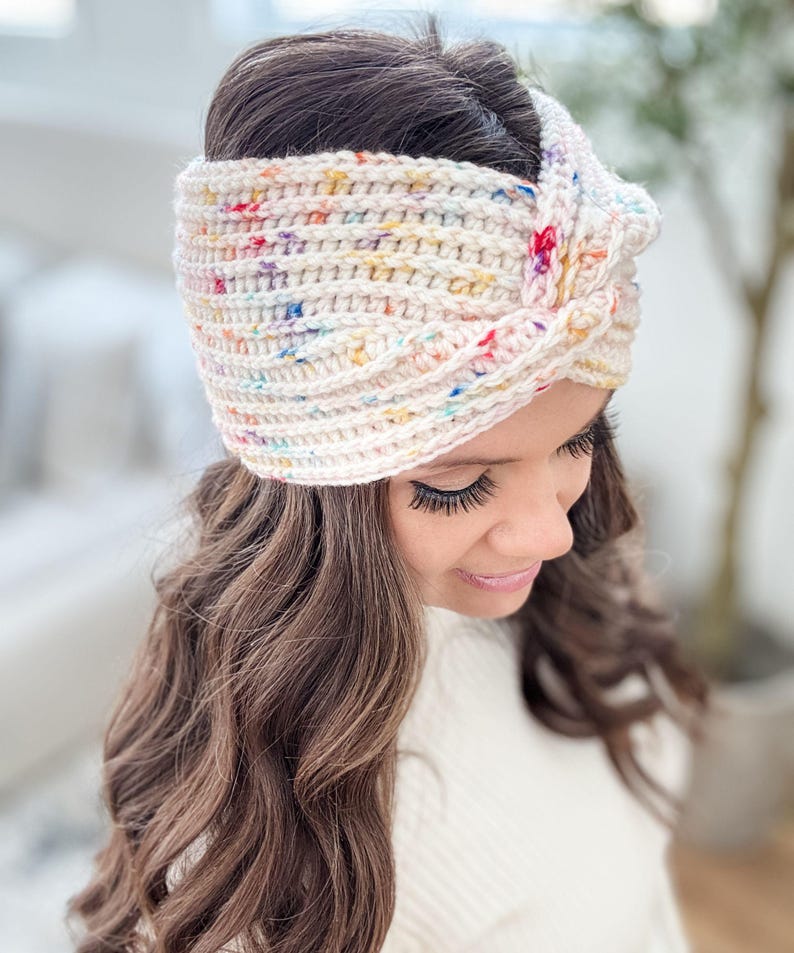 May include: A white crochet headband with a colorful confetti pattern. The headband is tied in a knot on top of the head.