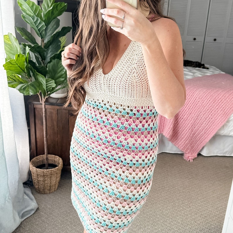 May include: A crochet dress with a white top and a multi-colored striped bottom. The dress is made with a granny square stitch and features pink, blue, and white colors.