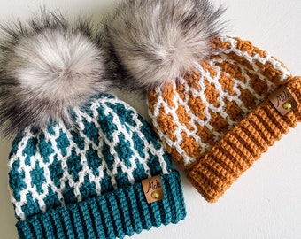 May include: Two crocheted hats with white and brown geometric patterns and faux fur pom poms. The hats have leather labels with the text "MJD's" on them.