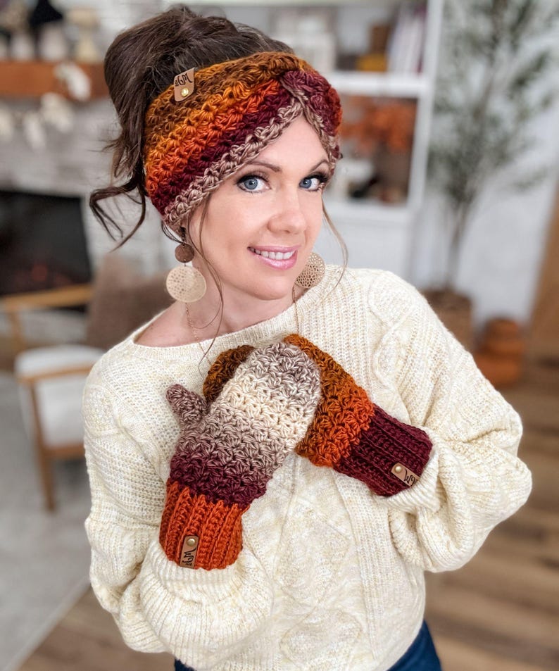 May include: A crocheted headband and mittens set in a fall color palette of orange, burgundy, and cream. The headband features a button detail, and the mittens have a matching design. The set is handmade and suitable for cold weather.