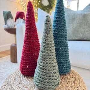 May include: Three crocheted Christmas trees in red, green, and blue. The trees are sitting on a woven rug.