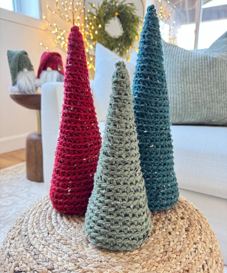 May include: Three crocheted Christmas trees in red, green, and blue. The trees are sitting on a woven rug.