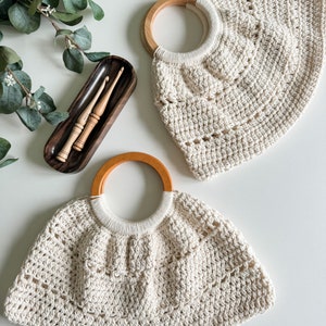 May include: Two crocheted bags with wooden handles. The bags are cream colored and have a textured, open weave. The bags are on a white surface.