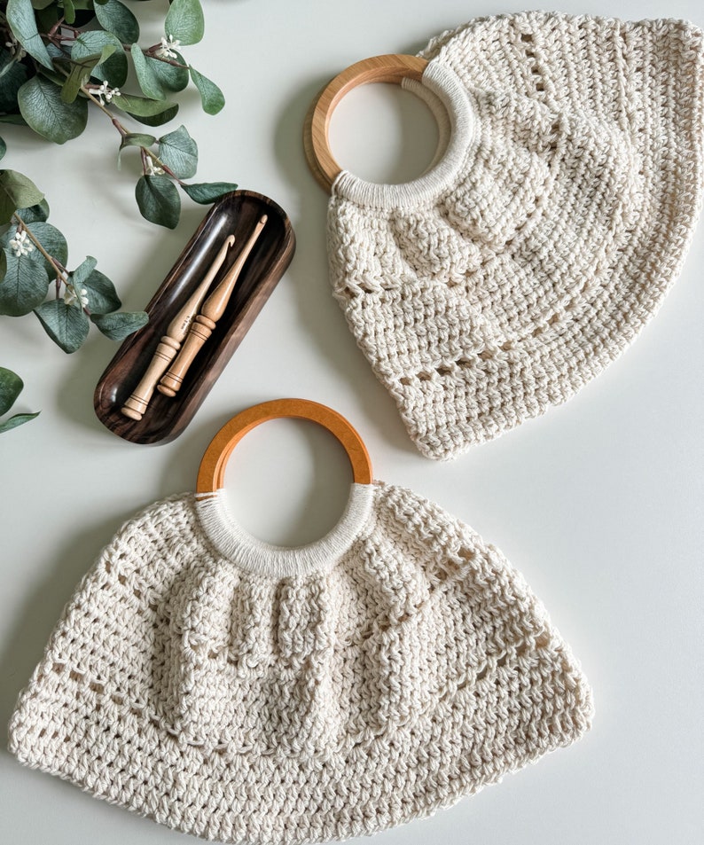 May include: Two crocheted bags with wooden handles. The bags are cream colored and have a textured, open weave. The bags are on a white surface.