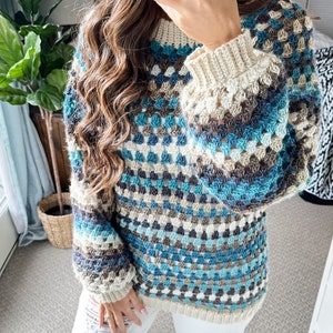 Pu&ograve; includere: Un maglione all'uncinetto fatto a mano con un motivo a granny square. Il maglione presenta un mix di filati blu, crema e marroni. Le maniche hanno un polsino pi&ugrave; ampio e lo scollo &egrave; a coste. &Egrave; un capo fatto a mano e accogliente.