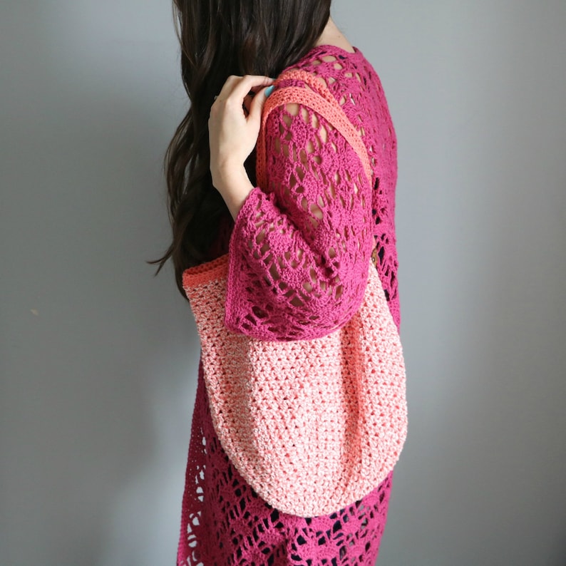 May include: A pink and coral crocheted tote bag with a long strap. The bag is being held by a person wearing a pink crocheted top.