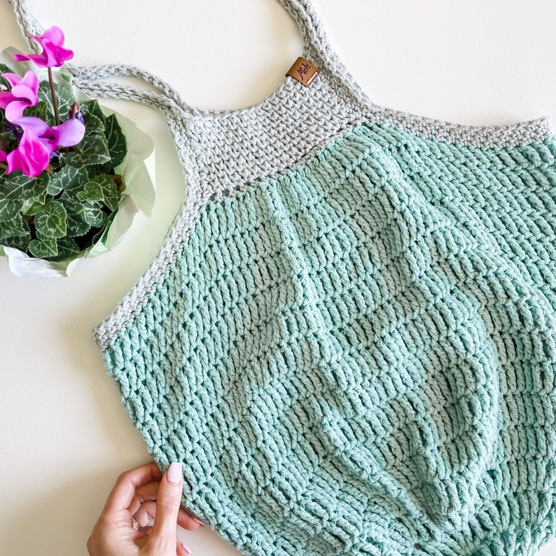 May include: A light green and gray crocheted tote bag with a brown leather tag that says "Joy".