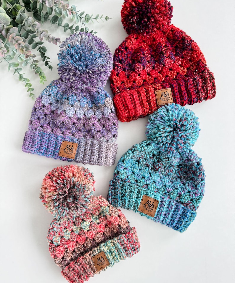 May include: Four colorful crocheted hats with pom-poms. Each hat has a brown leather tag with the text "Mels Handmade Designs".