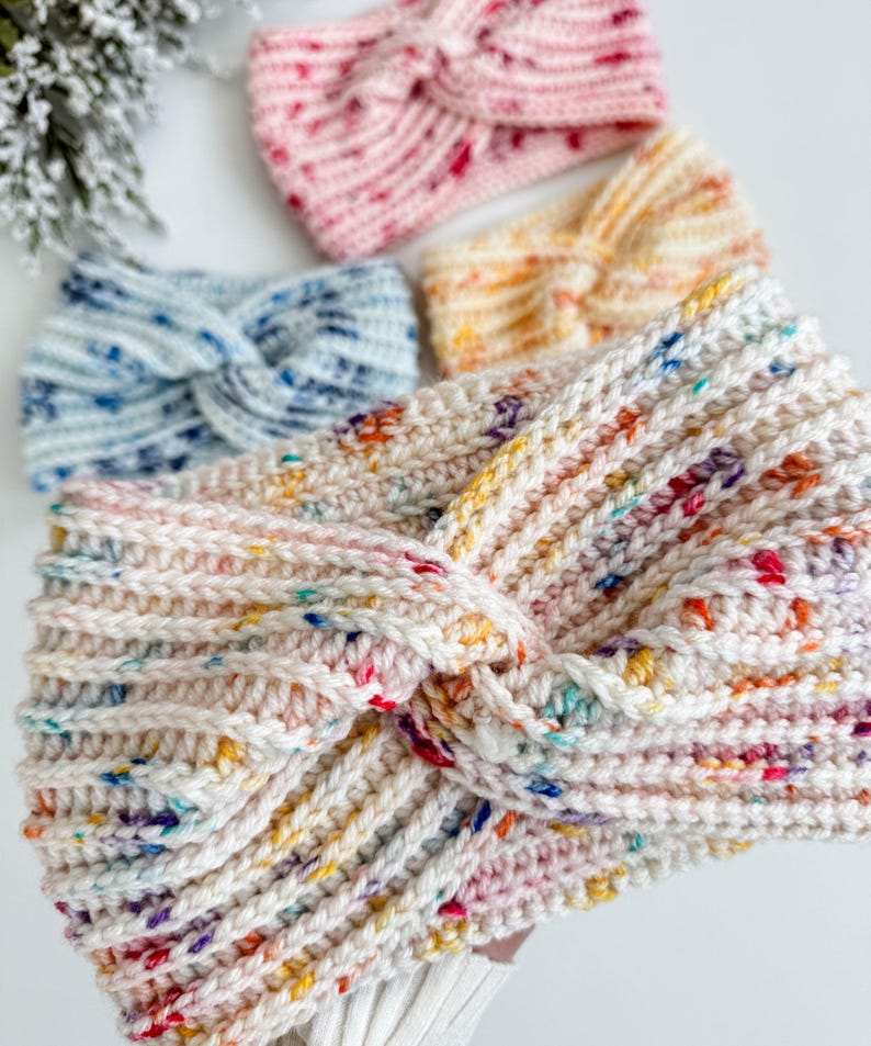 May include: Four crocheted headbands in different colors and patterns. The headbands are made with a chunky yarn and have a twisted knot design. The colors include pink, blue, yellow, and white.
