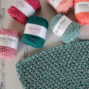 May include: Four balls of yarn in different colours: teal, pink, coral, and white and red striped. The yarn is labelled "Knit Picks Dishie Twist Worsted Weight".