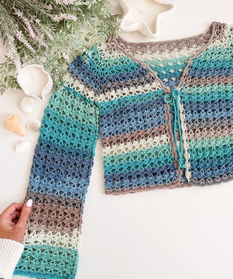 May include: A handmade, open-weave crochet cardigan in shades of blue, teal, and brown. The long-sleeved garment features a button closure and a delicate, airy design. The cardigan is a perfect addition to any wardrobe.