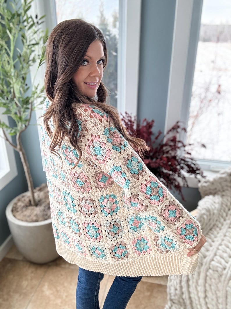 May include: A crocheted cardigan with a granny square pattern in shades of cream, pink, and blue. The cardigan has a long, loose fit and a V-neck.