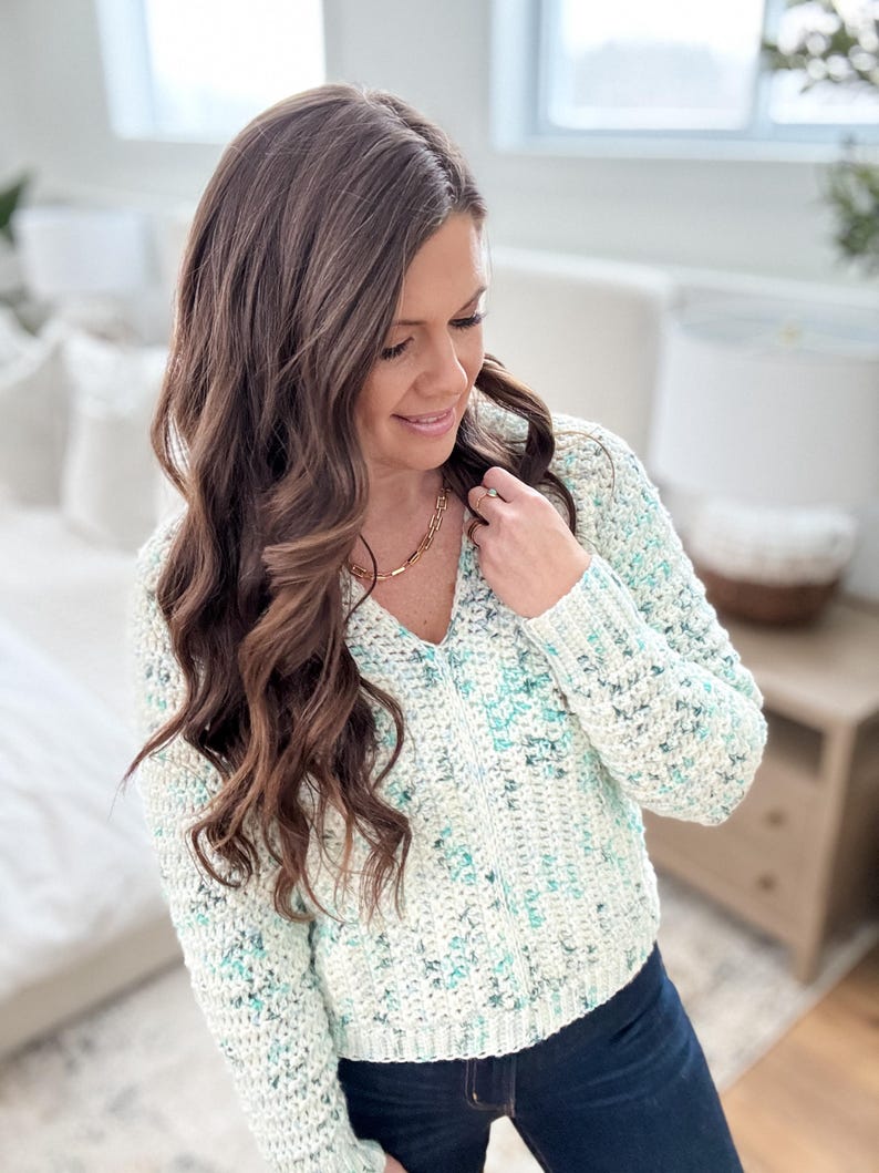 May include: A white and blue speckled crochet sweater with a v-neck and long sleeves.