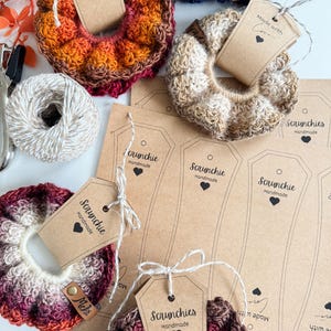 May include: A collection of handmade scrunchies in various colors, including orange, brown, and burgundy. Each scrunchie is made of a textured yarn and is attached to a tag that reads "Scrunchies Handmade". Some tags have the text "Made with Love".