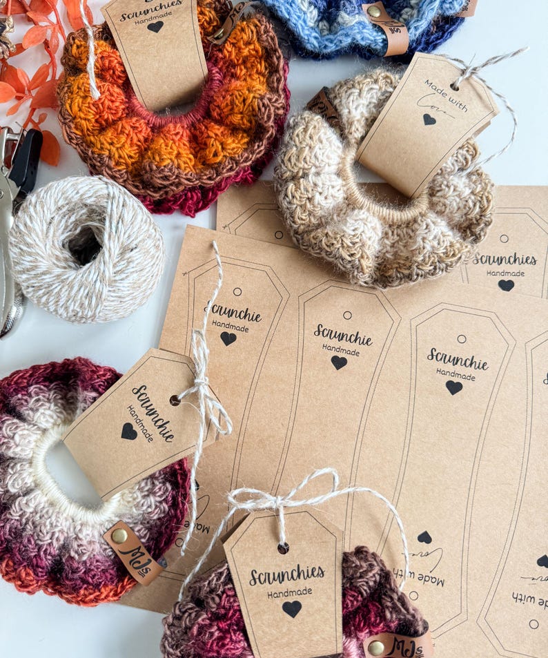 May include: A collection of handmade scrunchies in various colors, including orange, brown, and burgundy. Each scrunchie is made of a textured yarn and is attached to a tag that reads "Scrunchies Handmade". Some tags have the text "Made with Love".