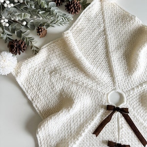 May include: A white knitted Christmas tree skirt with brown velvet ribbon bows. The skirt has a hole in the center for a tree stand.