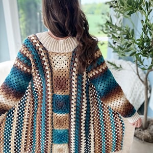 May include: A long, crocheted cardigan with a striped pattern in shades of brown, teal, and cream. The cardigan has a loose fit and a V-neck.