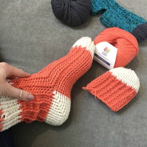 May include: A pair of orange and white striped knitted socks with a ball of orange yarn and a label that reads "Sugarbush Itty Bitty".