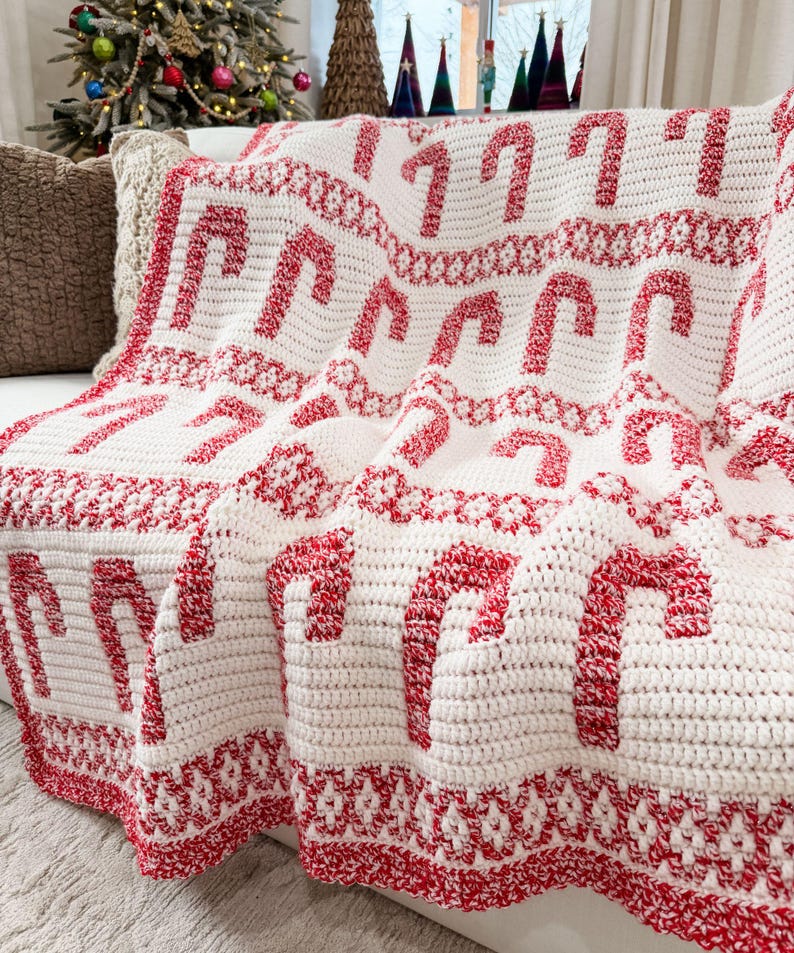 K&ouml;nnte beinhalten: Eine wei&szlig;-rote H&auml;keldecke mit einem Zuckerstangenmuster. Die Decke hat einen roten Rand und dekorative Elemente. Ideal f&uuml;r die Weihnachtszeit.
