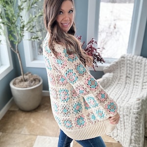May include: A cream-coloured crochet cardigan with a granny square pattern in shades of pink, blue, and brown. The cardigan has a long, open front and long sleeves.
