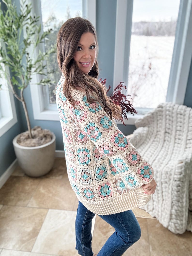 May include: A cream-coloured crochet cardigan with a granny square pattern in shades of pink, blue, and brown. The cardigan has a long, open front and long sleeves.