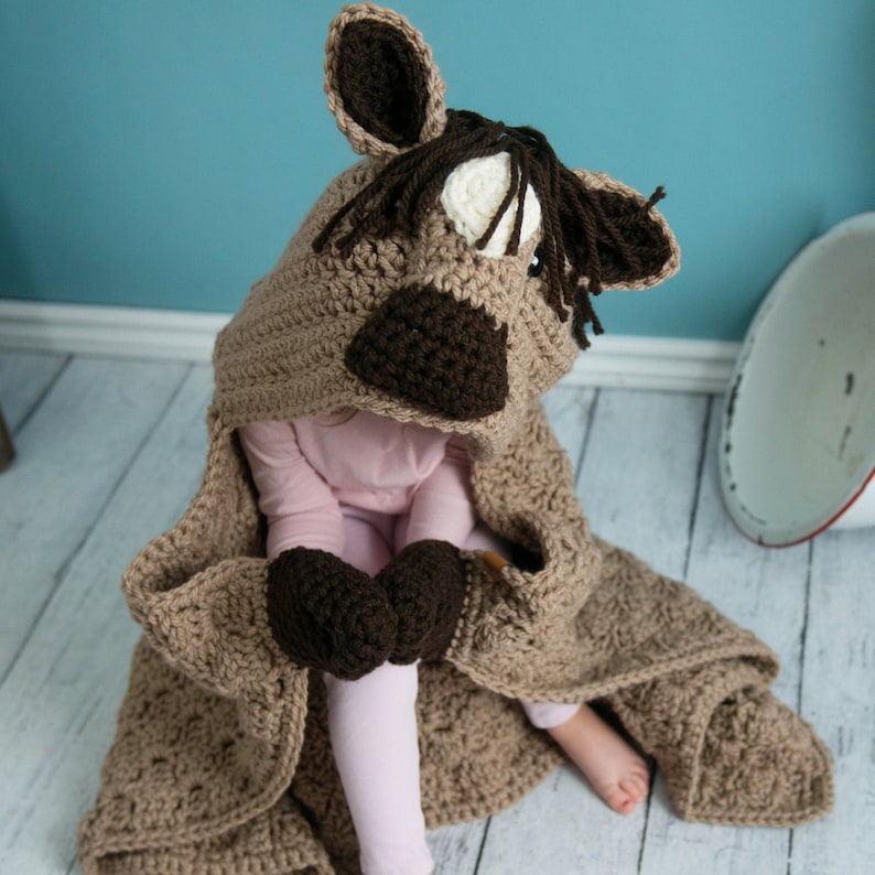 Pu&ograve; includere: Una coperta di cavallo in crochet marrone con cappuccio e guanti attaccati. La coperta &egrave; realizzata con un filato morbido e presenta un viso di cavallo dettagliato sul cappuccio.